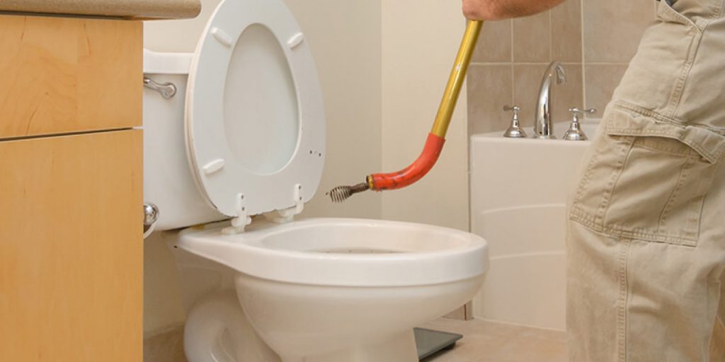 clearing a clogged toilet with a snake tool