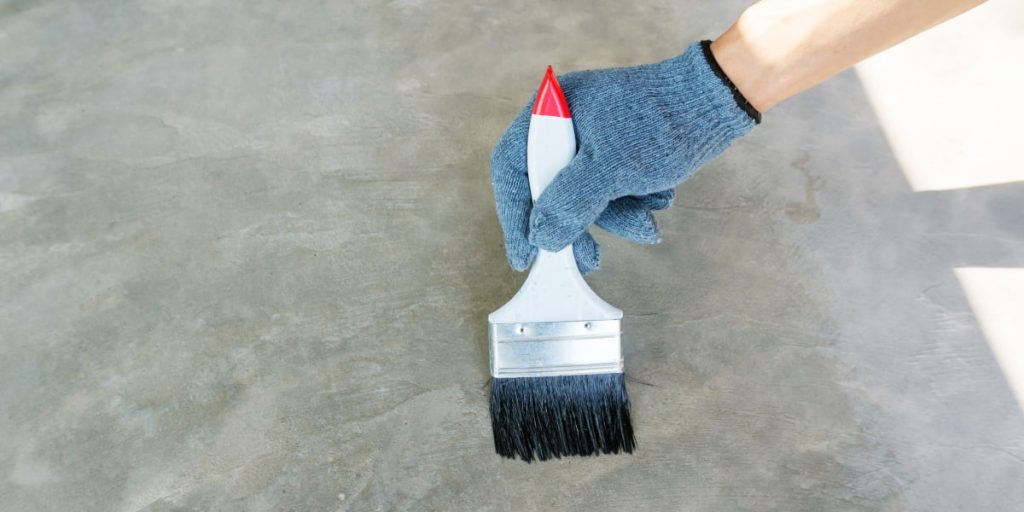 man with brush paint concrete floor basement